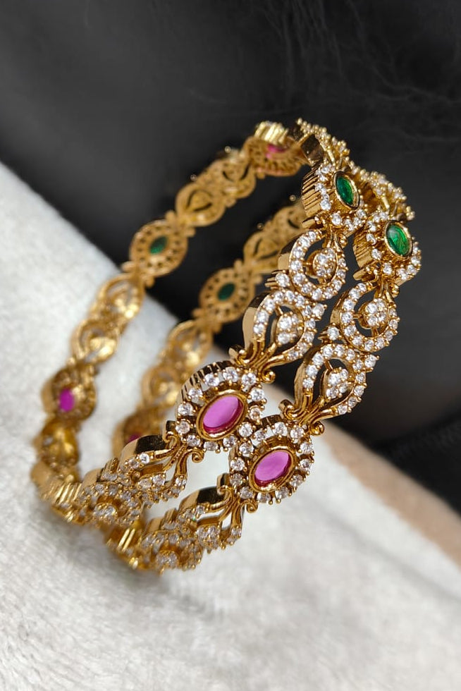 Gold bangles with zercon stones on a white fabric background